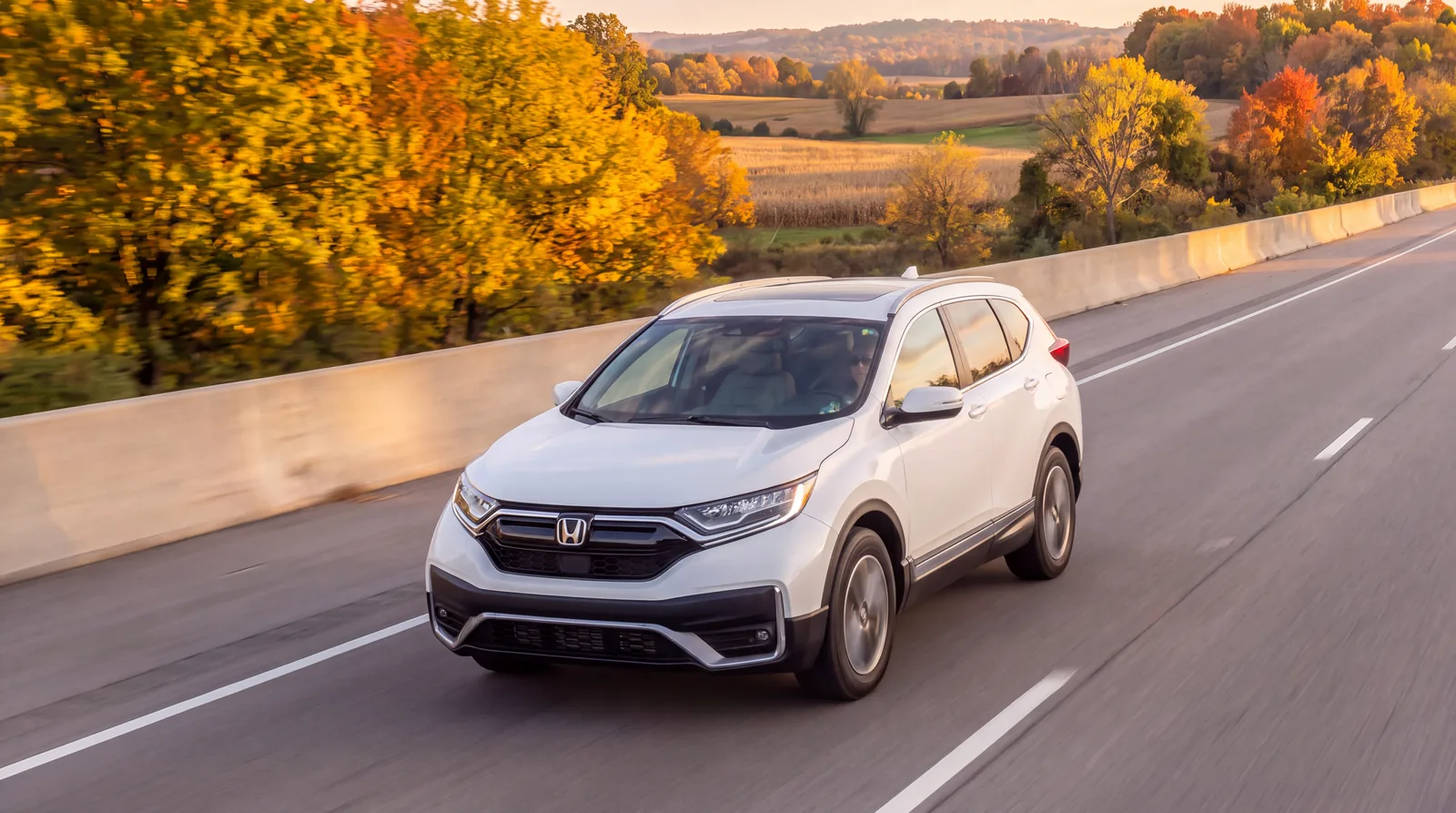 A white SUV driving on a highway past fall trees